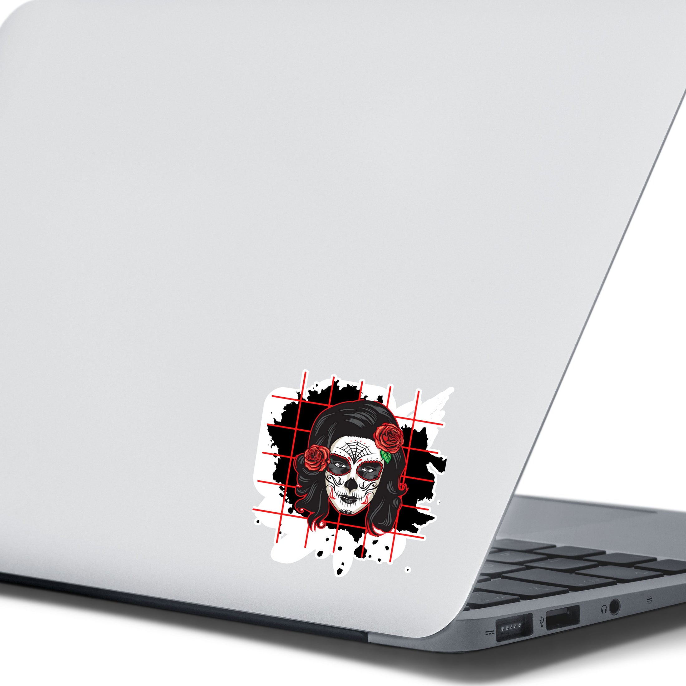 Trash Polka uses red, black, and white with a combination of abstract, surrealistic, and realistic images, and this individual die-cut sticker features a sugar skull woman with roses in her hair on a black background with a red grid. This image shows the trash polka sugar skull sticker on the back of an open laptop.