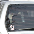 Load image into Gallery viewer, Trash Polka uses red, black, and white with a combination of abstract, surrealistic, and realistic images, and this individual die-cut sticker features a woman wearing sunglasses with her hair tied up on a white background with red swirls. This image shows the trash polka woman sticker on the back window of a car.

