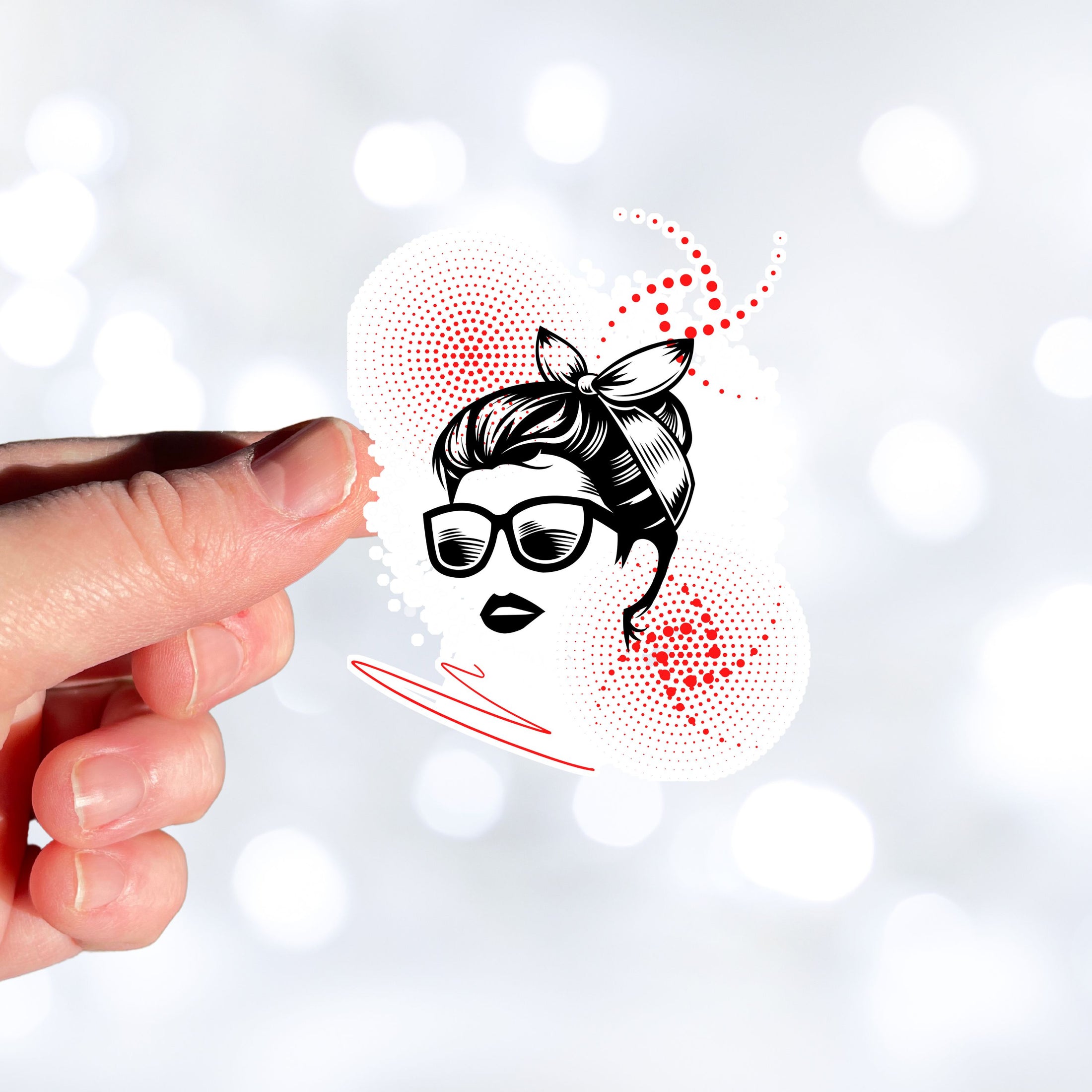 Trash Polka uses red, black, and white with a combination of abstract, surrealistic, and realistic images, and this individual die-cut sticker features a woman wearing sunglasses with her hair tied up on a white background with red swirls. This image shows a hand holding the trash polka woman sticker.