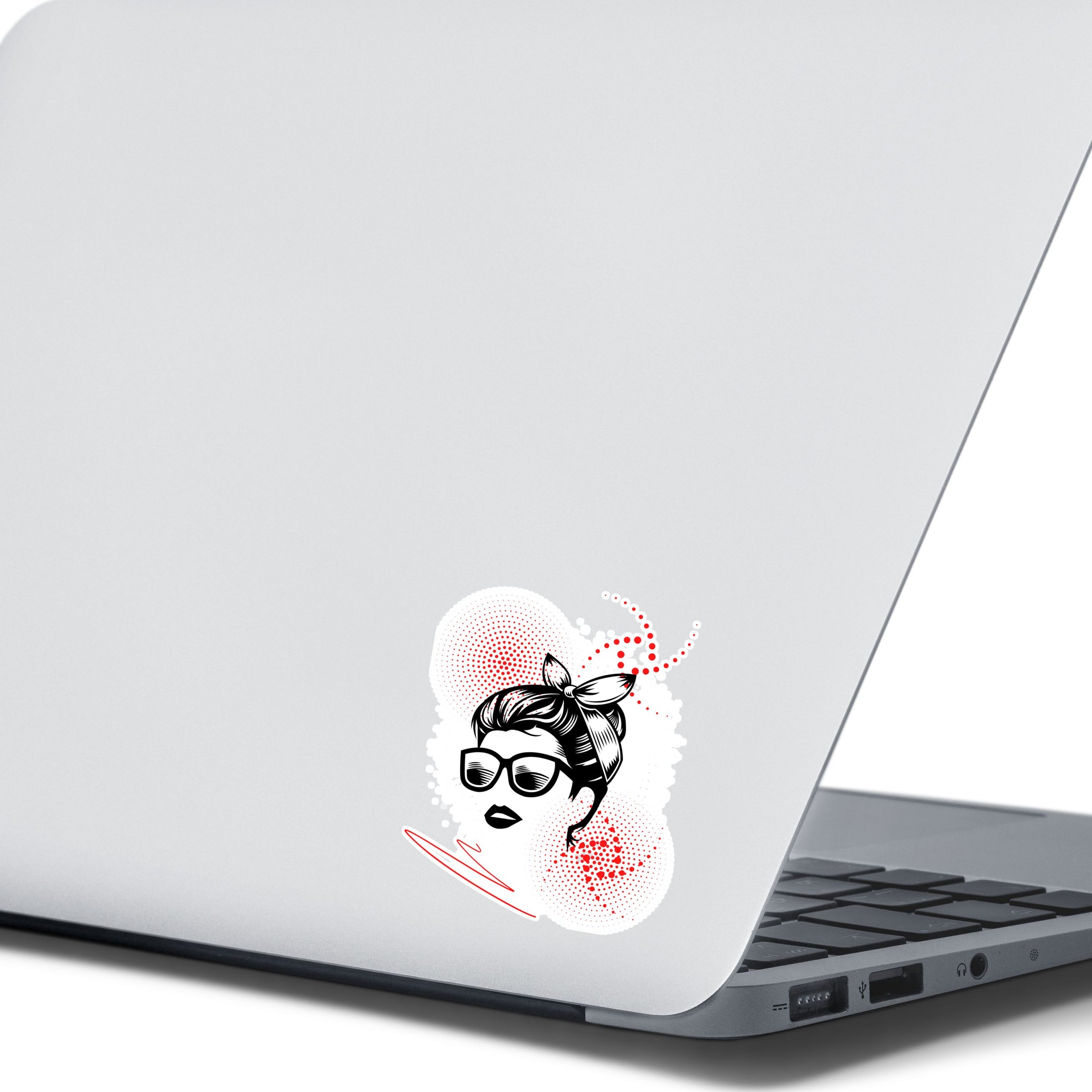 Trash Polka uses red, black, and white with a combination of abstract, surrealistic, and realistic images, and this individual die-cut sticker features a woman wearing sunglasses with her hair tied up on a white background with red swirls. This image shows the trash polka woman sticker on the back of an open laptop.