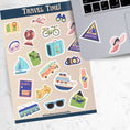 Load image into Gallery viewer, Pack your bags and grab your passport; it's travel time! This sticker sheet is filled with travel related sticker images sure to please even the most discerning traveler. Some of the sticker images are an airplane, suitcase, globe, and ship.  This image shows the sticker sheet next to an open laptop with a triangle sticker of a sailboat that says "Adventure", and a sticker of a pink floppy sun hat, applied below the keyboard.
