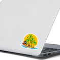 Load image into Gallery viewer, Pirate's Treasure awaits on this topical island! This individual die-cut sticker features an island with palm trees in front of the setting sun, and yes that is a treasure chest on the beach. But you'd better hurry before the pirate ship gets there and makes off with the prize! This image shows the Treasure Island sticker on the back of an open laptop.

