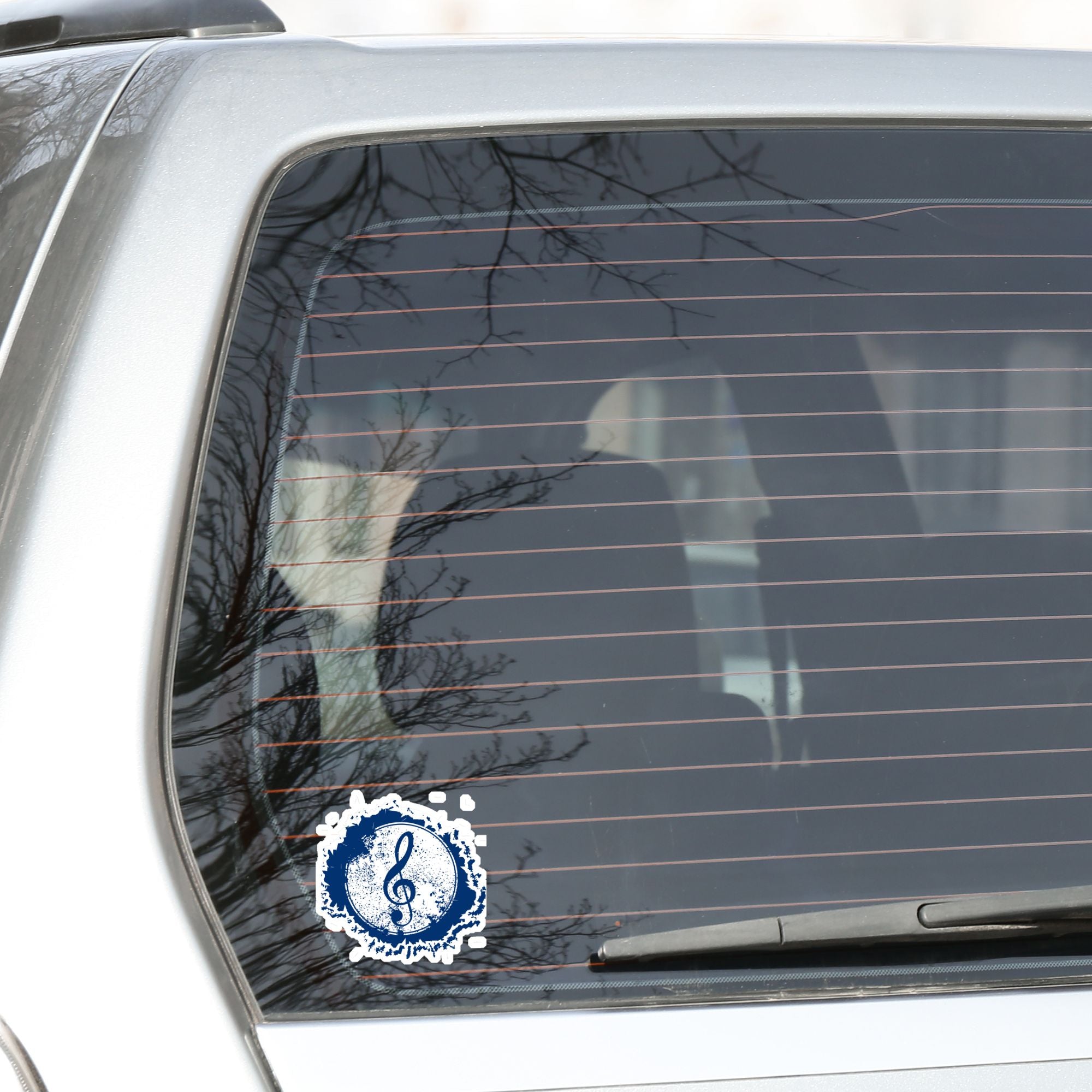 This individual die-cut sticker features a blue treble clef with a paint splattered background. Perfect for performers and music lovers alike!  This image shows the treble clef sticker on the back window of a car.