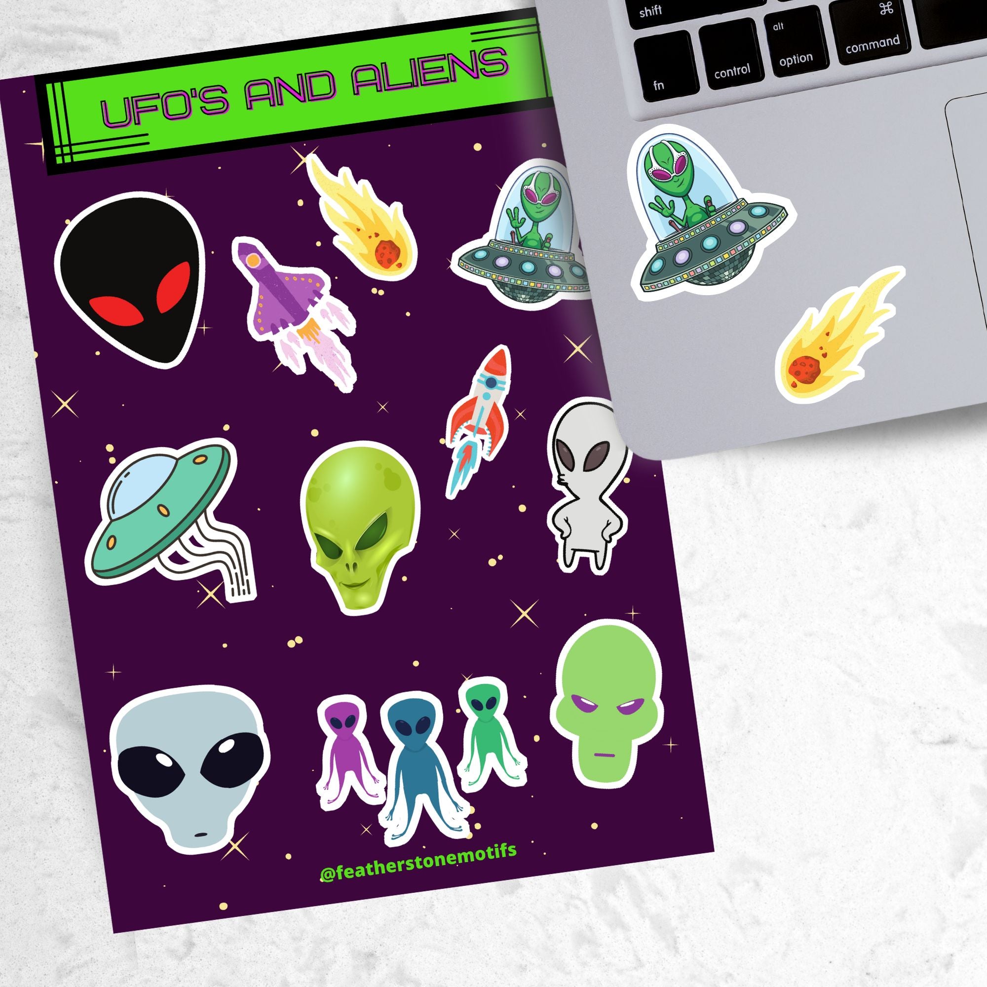 This sticker sheet is filled with aliens and UFOs with individual stickers of aliens, space ships, and alien creatures. This image is of a laptop with 2 of the individual stickers on it.