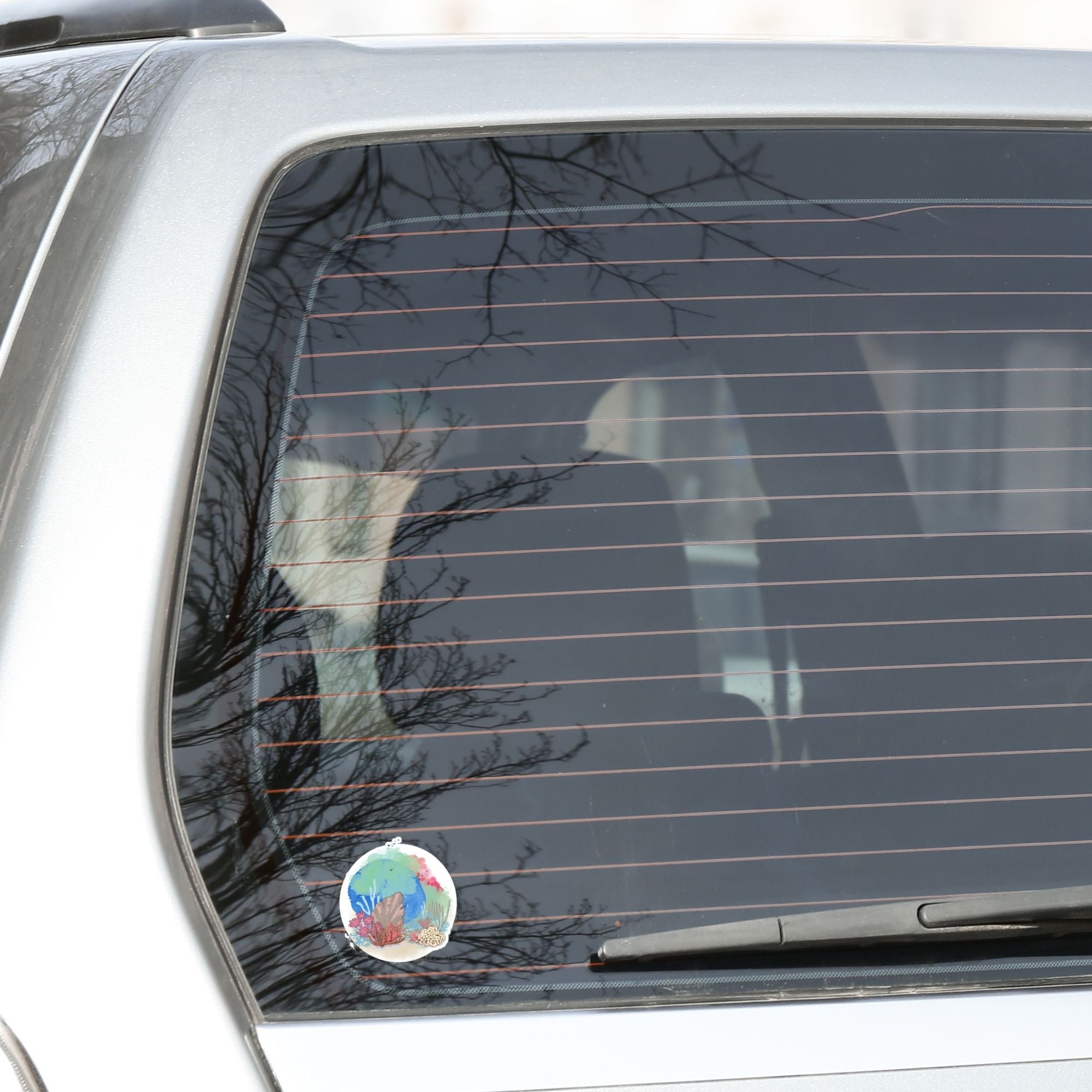 This underwater scene features corals, sand, and a pastel watercolor background on an individual die-cut sticker. With this sticker you can take the reef with you anywhere you go! This image shows the Watercolor Reef die-cut sticker on the back window of a car.