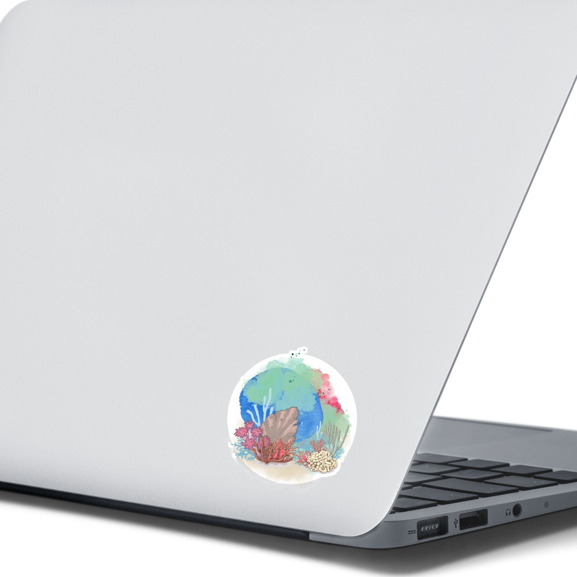 This underwater scene features corals, sand, and a pastel watercolor background on an individual die-cut sticker. With this sticker you can take the reef with you anywhere you go! This image shows the Watercolor Reef sticker on the back of an open laptop.