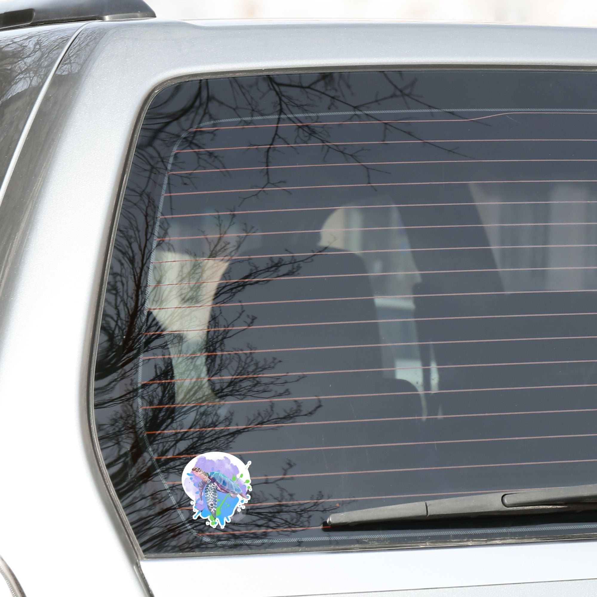 This individual die-cut sticker has a serene looking green sea turtle on a blue and purple background with splash of green. Just looking at this image is relaxing! This image shows the Watercolor Sea Turtle on the back window of a car. 