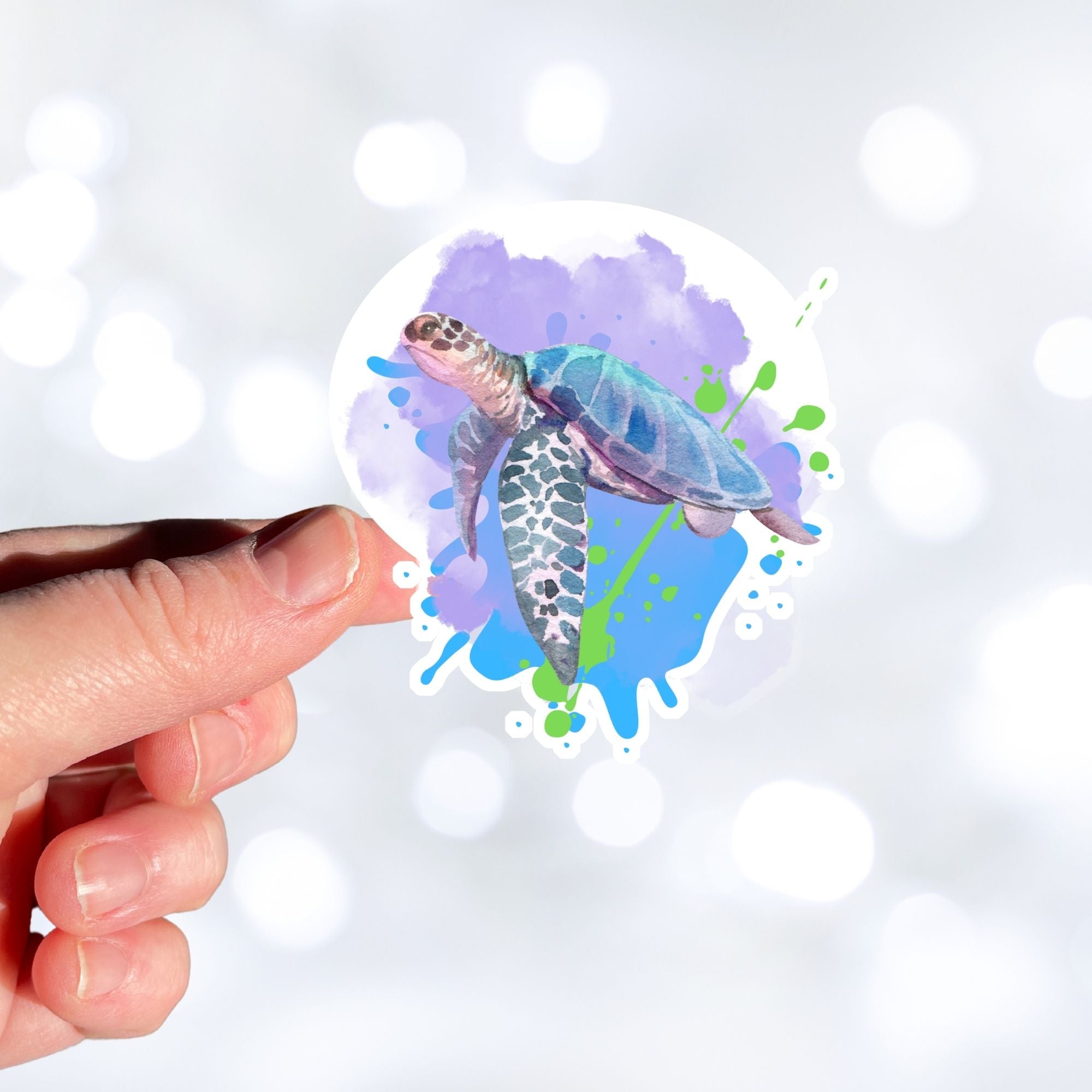 This individual die-cut sticker has a serene looking green sea turtle on a blue and purple background with splash of green. Just looking at this image is relaxing! This image shows a hand holding the Watercolor Sea Turtle sticker.