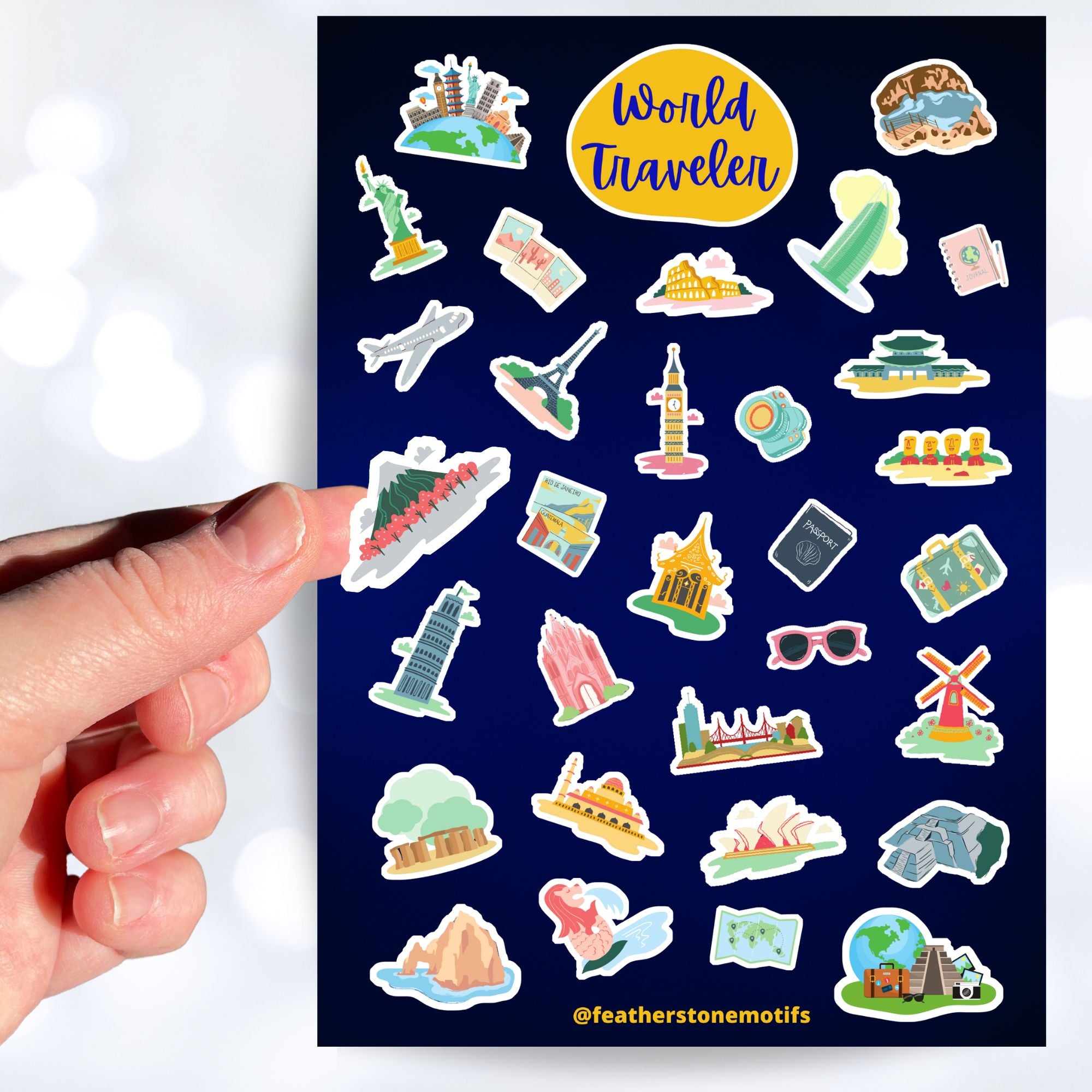 Our World Traveler sticker sheet has sticker images of iconic travel destinations! This sheet has a black background with over 30 different stickers including the Statue of Liberty, Easter Island, Stonehenge, and a passport and camera. This image shows a hand holding a sticker of a mountain above the sticker sheet.