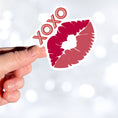 Load image into Gallery viewer, This individual die-cut sticker pretty much speaks for itself! It features a pair of lips with XOXO written above. Nuff said!  This image shows a hand holding the XOXO sticker.
