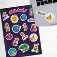 Load image into Gallery viewer, Sloth's on Bikes. Sloth's scuba diving. Sloth's relaxing. This sticker sheet is full of sticker images of sloth's doing all kinds of fun things! This image shows the sticker sheet next to an open laptop with stickers of a sloth floating on an air mattress with a drink, and a sloth on a jet ski, applied below the keyboard.

