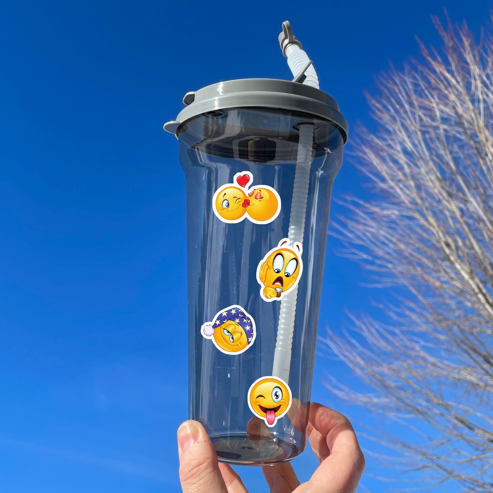 This sticker sheet features all your favorite smiley emojis! It's enough to make anyone smile! This image shows a water bottle with smiley faces kissing, a shocked smiley face looking at their watch, a sleepy smiley face, and a smiley face with their tongue hanging out.